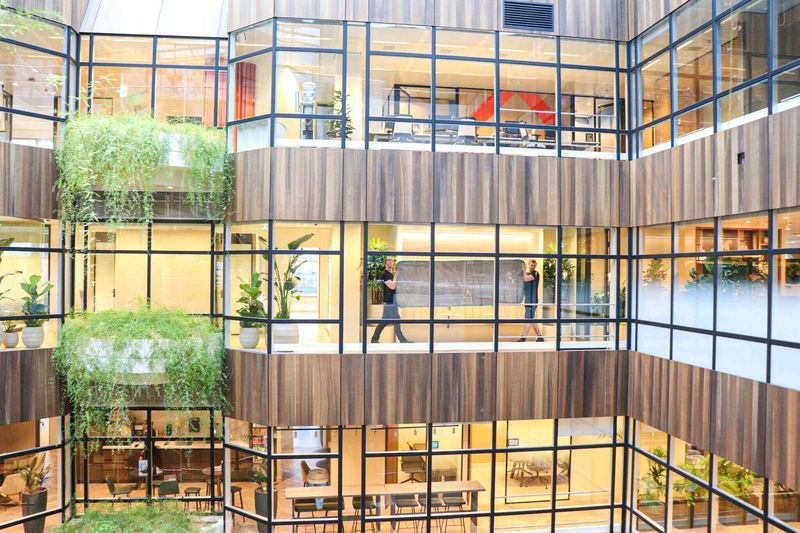 Twee medewerkers verplaatsen een beschermd meubel door een licht atrium met groen en houten wanden